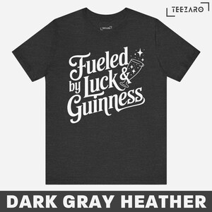 Puede incluir: Camiseta de color gris oscuro jaspeado con texto blanco que dice "Fueled by Luck & Guinness" con un vaso de Guinness estilizado y estrellas.