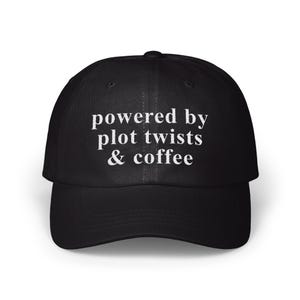 Puede incluir: Gorra de béisbol negra con el texto blanco "powered by plot twists & coffee". La gorra tiene una visera curva y una correa ajustable. Un accesorio casual para los amantes de la lectura y el café.