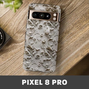 Puede incluir: Una funda de tel&eacute;fono blanca con un dise&ntilde;o floral en relieve 3D y un fantasma. La funda es para un tel&eacute;fono Pixel 8 Pro.