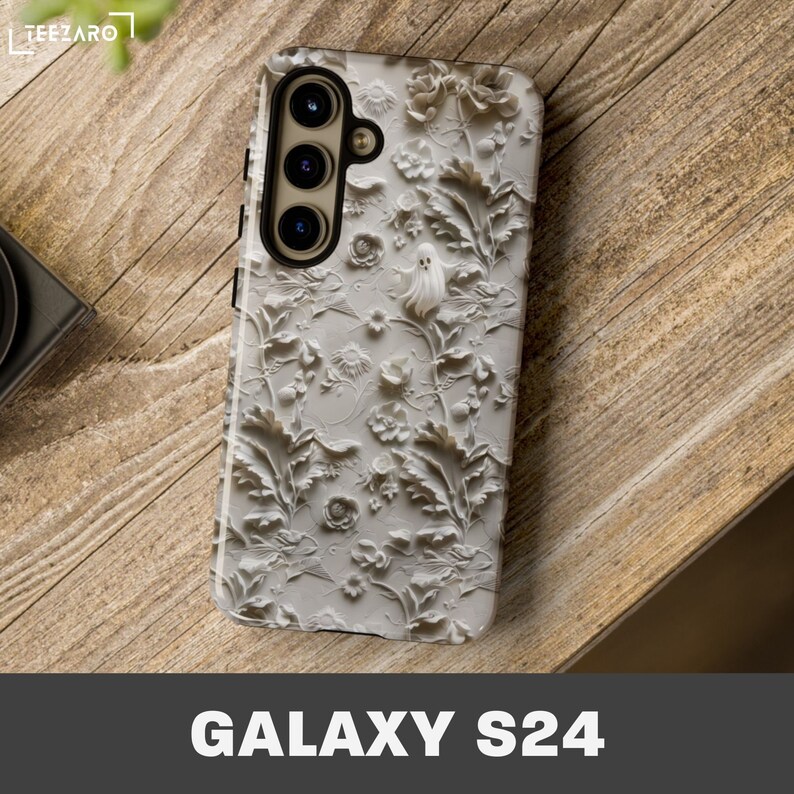 Puede incluir: Carcasa de tel&eacute;fono blanca con un dise&ntilde;o en relieve 3D de flores y un fantasma. La carcasa es para un tel&eacute;fono Galaxy S24.