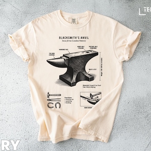 May include: Ivory-colored t-shirt featuring a detailed diagram of a blacksmith's anvil, including its parts and functions. The graphic is in black and white, with text labels. The shirt also includes the text "BLACKSMITH'S ANVIL" and "IVORY".