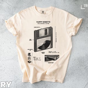May include: Ivory-colored t-shirt featuring a detailed diagram of a floppy disk, labeled "Floppy Diskette." The graphic includes dimensions (3.5 x 3.7 in), capacity, and format details. The shirt's design is a retro tech theme.