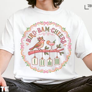 White t-shirt with "Bird Bam Cheers" text and illustration of birds toasting.