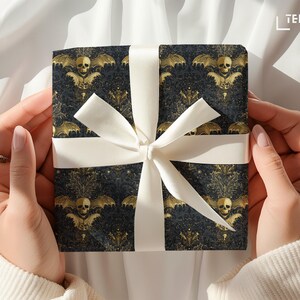 May include: A wrapped gift box with a black and gold bat and skull pattern, tied with a white satin ribbon. The gift box is held by hands, suggesting a present for a special occasion.