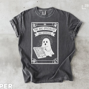 May include: Dark gray t-shirt with a white graphic featuring a ghost using a tablet. Text on the graphic reads "THE AAC SPECIALIST AAC ADVOCATE". The shirt has a crew neck and short sleeves. The word "TEEZARO" is in the upper right corner.