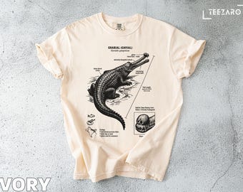 Może przedstawiać: Kremowa koszulka z szczegółową czarno-białą ilustracją gawiala, z naukowymi adnotacjami. Koszulka zawiera tekst "GHARIAL (GAVIAL)" i "IVORY" na dole. Gawial jest przedstawiony ze swoim charakterystycznym długim pyskiem.
