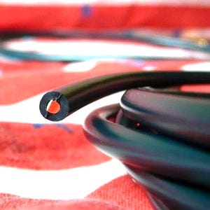 May include: Close-up of a black electrical cable with a red interior. The cable is coiled, with a cut end showing the internal wiring. The background is a red and white patterned fabric.