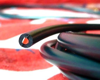 May include: Close-up of a black electrical cable with a red interior. The cable is coiled, with a cut end showing the internal wiring. The background is a red and white patterned fabric.