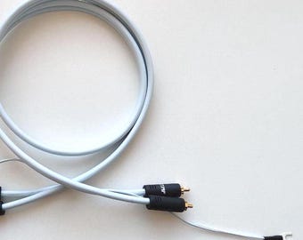May include: A white audio cable with black connectors and gold-colored tips. The cable is coiled in a loop and has two separate ends with exposed wires. The connectors are labeled with text.