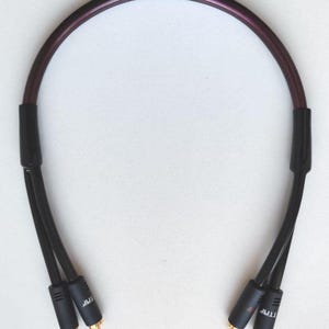 May include: A black and purple audio cable with gold-coloured connectors. The cable is curved, with black connectors at each end. The connectors have the text "TNR" printed on them.