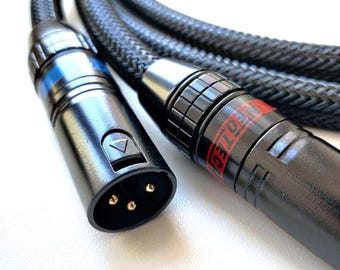 May include: Close-up of two black audio cables with silver and gold connectors. The cables have a braided black exterior. One connector has a blue ring and a triangle button. The other connector has red text.