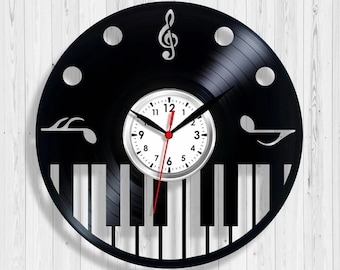 May include: A black vinyl record clock with a white clock face and red second hand. The clock features a piano keyboard design at the bottom and musical notes and a treble clef cut out of the record. The clock is mounted on a white wooden background.