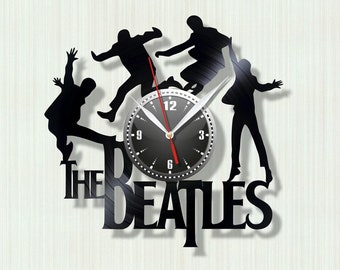 May include: Black wall clock featuring a silhouette of The Beatles with a clock face in the center. The clock hands are red and the numbers are white. The band's name is displayed in large, bold letters below the clock.