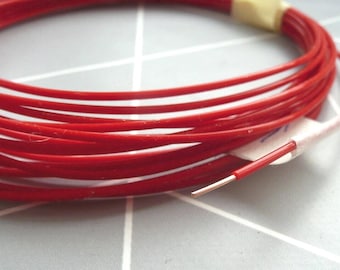 May include: Coiled red electrical wire with a single exposed wire end. The wire is wrapped with a white label and tape. The wire is a bright, solid red color.