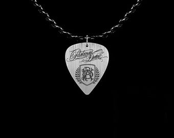 May include: A silver guitar pick pendant with the words "Parkway Drive" in script and a crest design. The pendant hangs from a black chain against a black background. The pick is approximately 1.25 inches long.