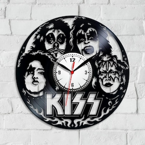 Puede incluir: Reloj de vinilo negro con la banda KISS. La esfera del reloj es blanca con números y manecillas negros. Las caras de los miembros de la banda están recortadas del disco de vinilo, con el nombre de la banda en letras blancas debajo.