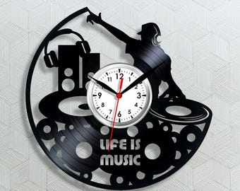 May include: Black vinyl record clock featuring a DJ silhouette with headphones, turntables, and speakers. The clock face is white with black numbers and hands. The text "LIFE IS MUSIC" is displayed on the record.