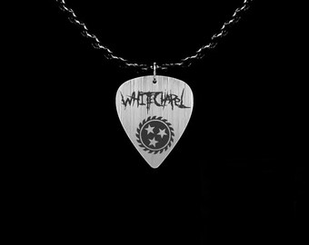 May include: Silver-colored guitar pick pendant with the band name "WHITECHAPEL" in a gothic font. Below the name is a circular design with three stars. The pendant hangs from a black chain.