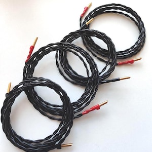 May include: Four black speaker wires with gold connectors and red heat shrink tubing, coiled into loops. The wires are designed for audio equipment. The image is set against a white background.