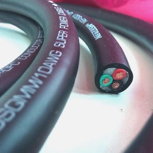 May include: A close-up of a black and burgundy power cable with the text "SUPER POWER CABLE" and "1DAWG". The cut end shows four coloured wires: red, green, and two copper-coloured wires. The cable is for electrical applications.