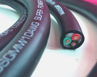 May include: Close-up of a black and burgundy power cable with the text "SUPER POWER CABLE" and "1DAWG". The cut end reveals four colored wires: red, green, and two copper-colored wires. The cable is designed for electrical applications.