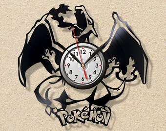 May include: Black vinyl record clock featuring a stylized Charizard design with outstretched wings. The clock face is white with black numbers and hands, and a red second hand. The word "Pokémon" is at the bottom.