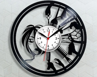 May include: A black vinyl record clock featuring a white clock face with black numbers and red hands. The clock's design includes silhouettes of hairdressing tools like scissors, combs, and a stylized female face, perfect for a salon or barber shop.