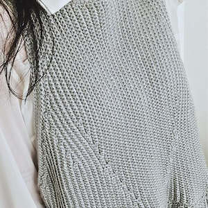 May include: A gray knitted sleeveless top with a ruffled hem.