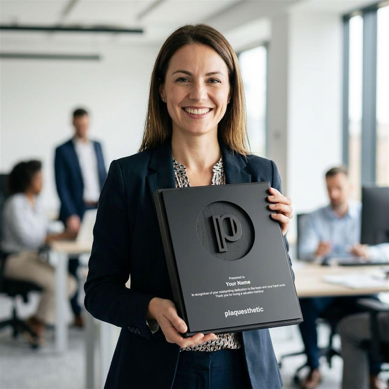 May include: A woman holds a black plaque with a raised "p" logo and the text "plaquesthetic." The plaque also includes the text "Presented to Your Name" and a dedication. The woman is wearing a navy blazer.