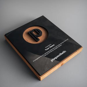 May include: A black plaque with a wooden frame and a silver inscription. The plaque features a circle with a wooden background and a black letter "P" in the center. The inscription reads "Presented to Your Name In recognition of your outstanding dedication to the team and your hard work. Thank you for being a valuable member. plaquesthetic"