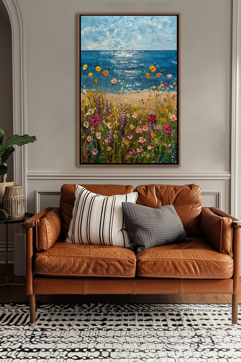 Puede incluir: Pintura al &oacute;leo de una escena costera con cielo azul y mar. El primer plano presenta una playa de arena con coloridas flores silvestres en tonos rosa, amarillo y morado. La obra est&aacute; enmarcada en un marco de madera marr&oacute;n.