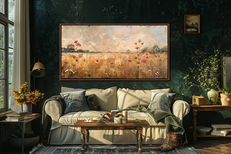 May include: A painting of a field with wildflowers in shades of pink and white, set against a backdrop of a cloudy sky. The painting is framed in a dark wood frame and hangs on a dark green wall in a living room setting.