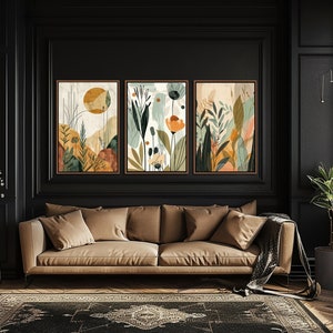 May include: Three framed abstract art prints with a nature theme. The prints feature a mix of green, brown, orange, and yellow colours. The prints are hung on a black wall above a brown sofa.