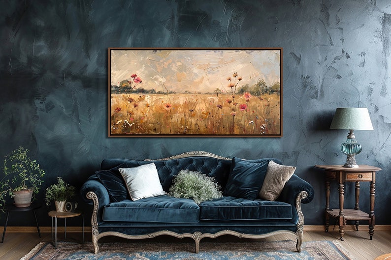 May include: A framed oil painting depicting a field of wildflowers in shades of pink, yellow, and green. The painting is set against a backdrop of a cloudy sky and is displayed on a wall in a living room setting.