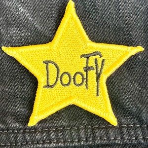 May include: A yellow star-shaped patch with the word "Doo-Fly" embroidered in black thread.