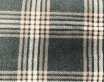 May include: Close-up of a plaid fabric in shades of gray, beige, and white. The pattern features a classic grid design with intersecting vertical and horizontal lines, creating a textured appearance. The fabric has a soft, inviting look.