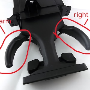 May include: A black plastic device with two curved arms extending from the sides. The device has a rectangular base and a central support structure. The arms are smooth and rounded, and the overall design is functional.