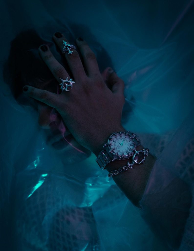 Puede incluir: Un reloj de pulsera plateado con una esfera blanca y agujas negras. El reloj tiene una correa plateada con un brazalete de cadena plateada unido a &eacute;l. El reloj se lleva en la mu&ntilde;eca de una persona.