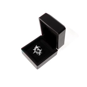 Puede incluir: Un anillo de plata con un dise&ntilde;o de coraz&oacute;n en una caja de anillo de terciopelo negro.