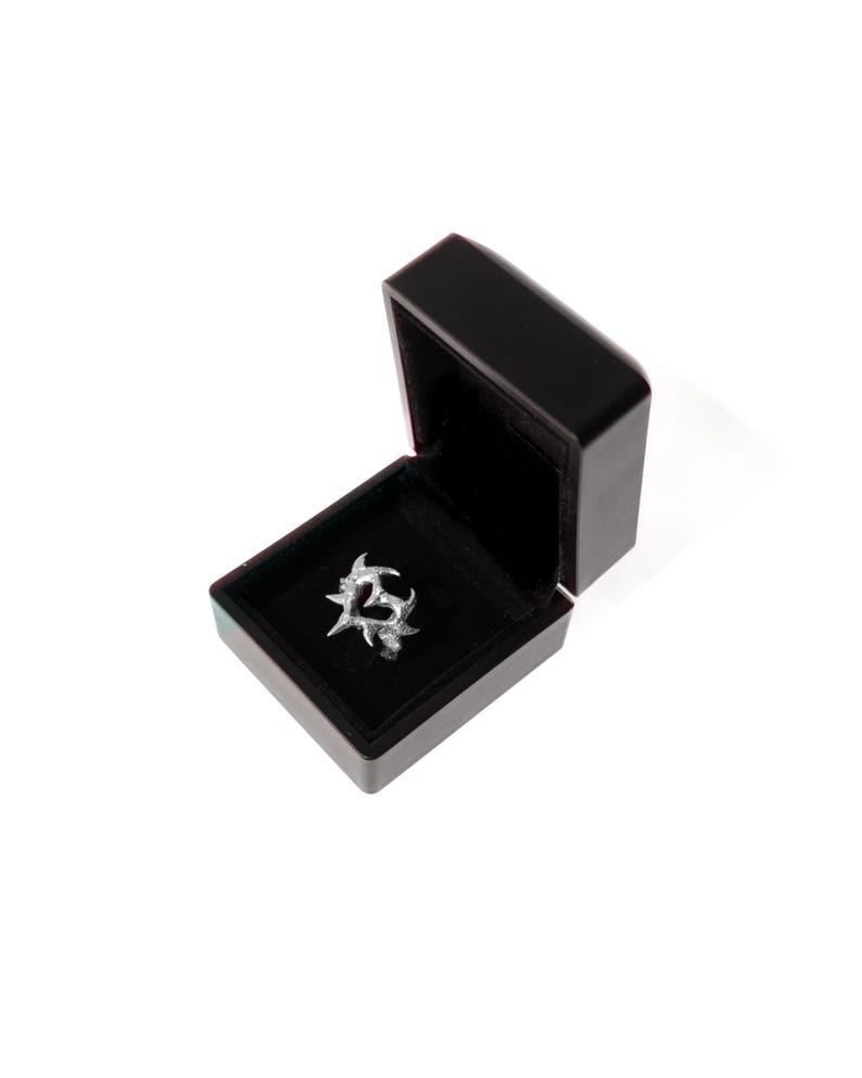 Puede incluir: Un anillo de plata con un dise&ntilde;o de coraz&oacute;n en una caja de anillo de terciopelo negro.