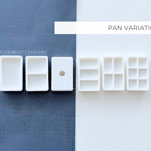 May include: White paint pans in various configurations are displayed against a blue and white background. The text "PAN VARIATIONS" is above the pans. The pans are rectangular with multiple compartments for holding paint.