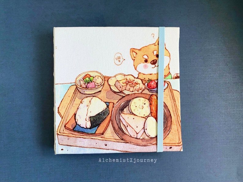 Może przedstawiać: Biały notes z pł&oacute;tna z ilustracją brązowej drewnianej tacy z r&oacute;żnymi japońskimi potrawami, w tym onigiri, tofu i miską zupy. Pies rasy Shiba Inu zagląda zza tacy, wyglądając na ciekawego. Notes ma niebieską wstążkę zamykającą i napis "AlchemistXJourney" wydrukowany na dole.