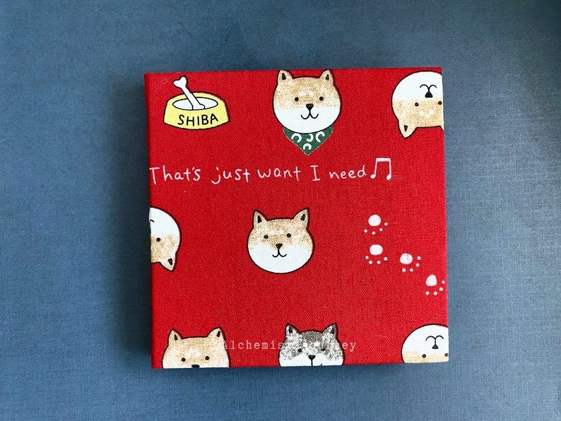 Może przedstawiać: Czerwony notes z tkaniny z wzorem psa rasy Shiba Inu. Na notesie widnieje napis "That's just want I need".