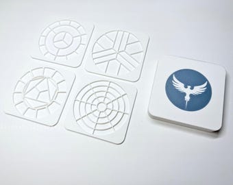 May include: A collection of white, geometric design stencils and a square coaster. The stencils feature various patterns, including circles and geometric shapes. The coaster has a blue circle with a white bird emblem.