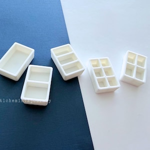 Puede incluir: Cinco paletas de pintura de acuarela rectangulares blancas con configuraciones de compartimentos variables, incluyendo diseños de uno, dos, tres y seis pocillos. El texto AlchemistJourney está impreso en letras grises pequeñas en la parte inferior izquierda.