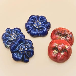 May include: Four ceramic flower buttons, two blue and two red. The blue buttons have a gold center and the red buttons have a gold center and gold accents.