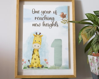 May include: A framed print featuring a yellow giraffe, a small brown bird, and the number one in a soft blue watercolor style. The text reads One year of reaching new heights. The frame is light wood and the artwork has a white background with flowers.
