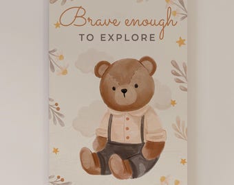 May include: A rectangular wall art print featuring a brown teddy bear wearing a light beige shirt and dark brown overalls. The text "Brave enough TO EXPLORE" is printed above the bear, surrounded by illustrations of small yellow stars and leaves.