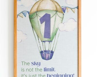 May include: A framed print featuring a watercolor hot air balloon in shades of green and tan with a large purple number one on the front. The background is light blue with white clouds and bunting. Text reads: The sky is not the limit it's just the beginning!