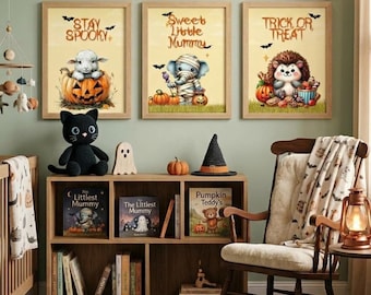 May include: Three framed wall art prints featuring a lamb in a pumpkin, an elephant mummy, and a hedgehog with the text Stay Spooky, Sweet Little Mummy, and Trick or Treat. A black crochet cat, books, and a witch hat sit on a wooden shelf.
